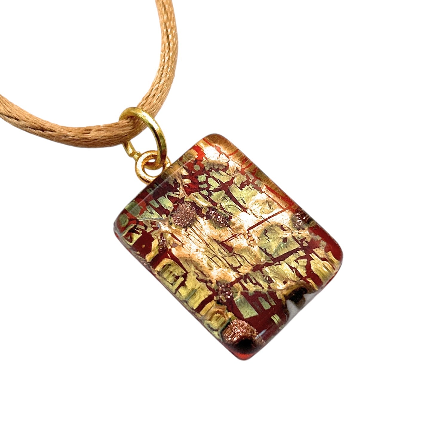 A close-up of the Murano Passion Glass Pendant, Green on Gold Leaf - Dainty 2cm x 1.5cm (MGPP12), reveals a rectangular piece featuring a rich mix of gold, bronze, and copper-colored abstract patterns on a glossy surface. It hangs elegantly from a caramel-colored cord and comes with a Certificate of Authenticity as part of Murano Glass Jewellery.