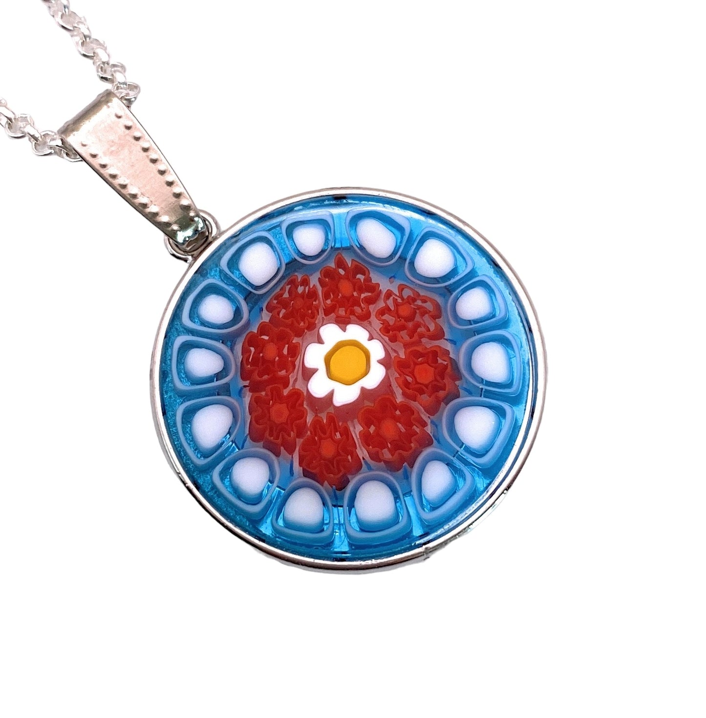 The Murano Passion pendant, crafted from Murano glass with a Millefiori floral design, features a central yellow flower encircled by vibrant red petals, bordered by blue and white petal-like shapes. This 2.4cm piece of Venetian artistic heritage elegantly hangs on a silver chain.