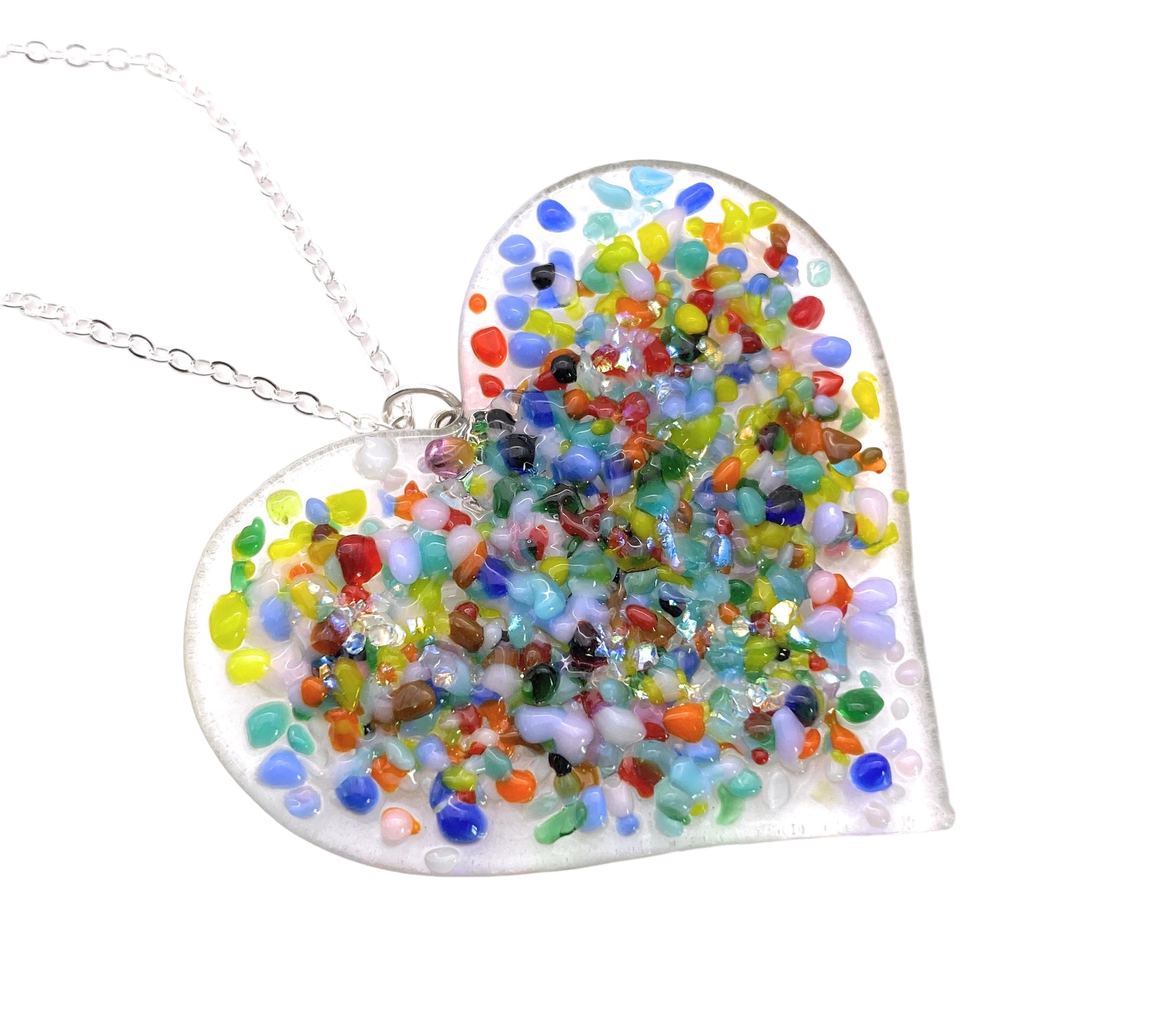 Introducing the Chunky Handmade Heart Pendant by Calon Glass, a stunning accessory featuring a silver chain and handmade dichroic glass. This heart-shaped pendant measures 6cm by 4cm and showcases a vibrant mosaic pattern with colorful pieces in green, blue, red, yellow, and orange on a clear background. The iridescent charm of the dichroic glass adds an exquisite touch to this beautiful piece.