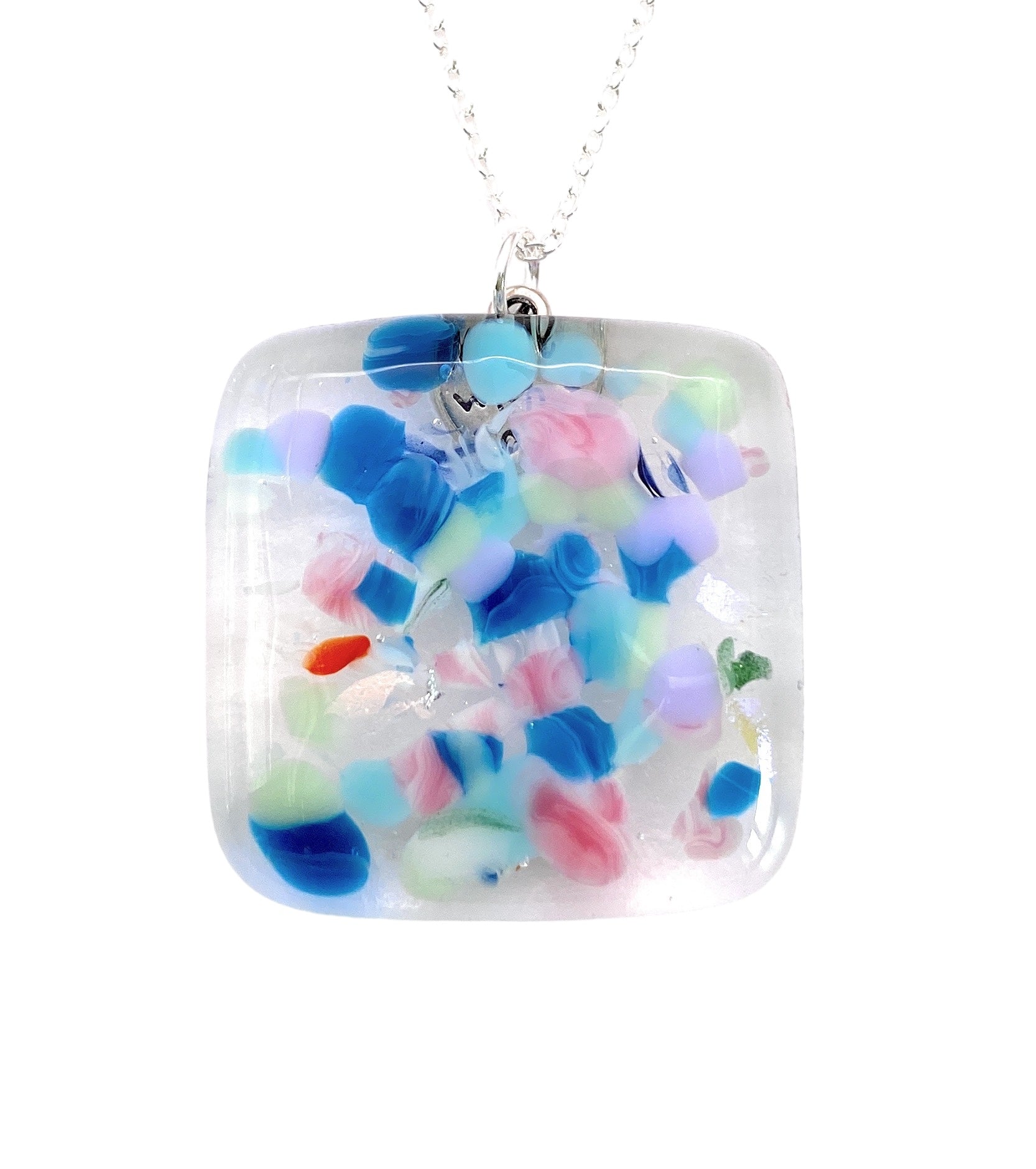 This exquisite pendant necklace from Calon Glass features a Handmade Dichroic Glass Pendant adorned with a rainbow mosaic design in vibrant blue, pink, and green abstract patterns set against a clear background. The 3cm x 3cm square charm gracefully hangs from a delicate silver chain.