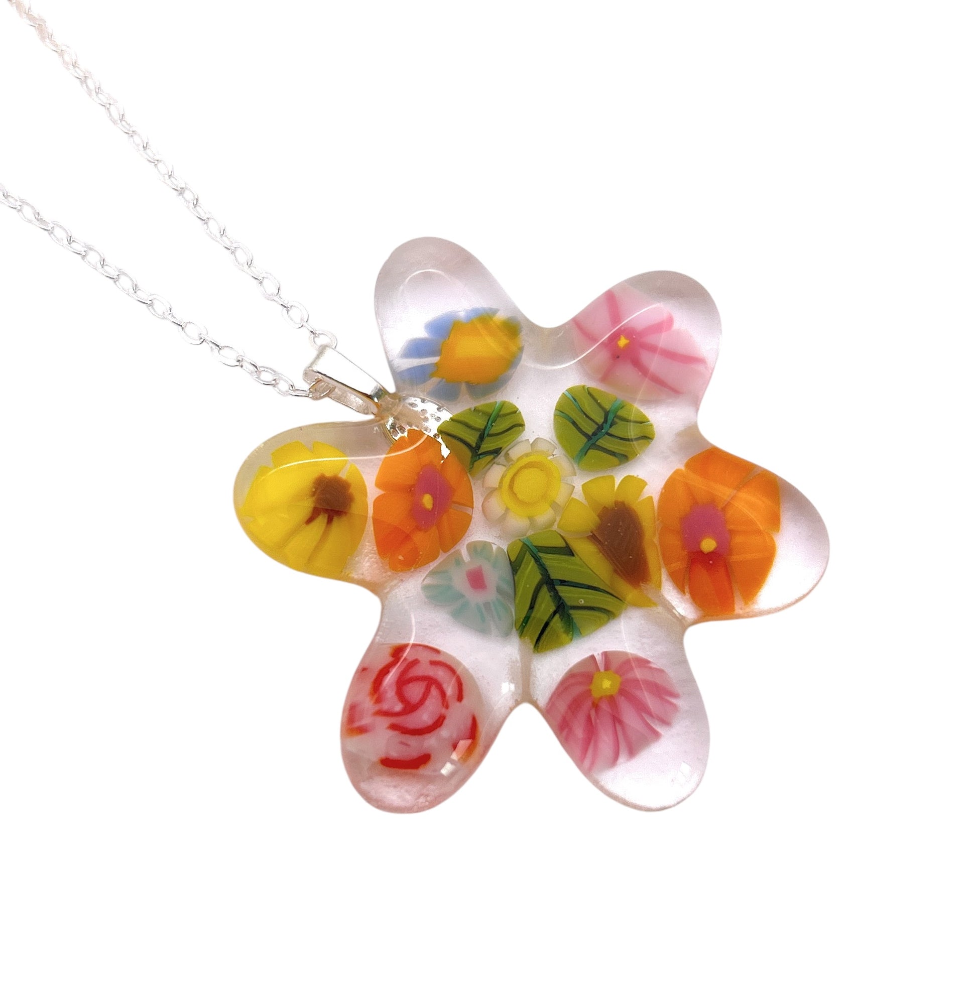 The Handmade Glass Pendant by Calon Glass, known as the Millefiori Flower Pendant - Chunky 4.5cm x 4cm (CGP31), showcases an intricate design of colorful Millefiori glass flowers and leaves set in clear resin. It is suspended from a delicate silver chain against a white background.