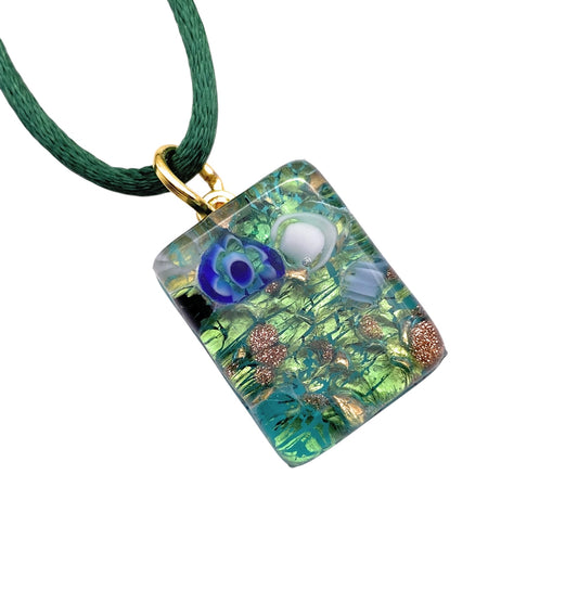 The Murano Passion MGPP34 Pendant features a 2cm x 1.5cm rectangular charm with intricate green and blue abstract floral and leaf designs on gold leaf, attached to a dark green cord. It's part of the Murano Glass Jewellery collection, complete with a Certificate of Authenticity.