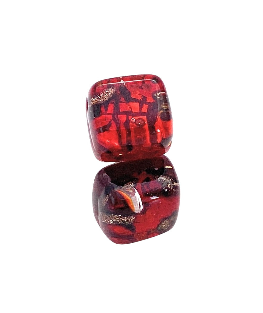 Two Murano Passion translucent red dice with dark patterns rest on a white background, reminiscent of the intricate swirling textures found in the Murano Glass Stud Earrings, Red on Gold Leaf. Each die displays unique patterns inside, echoing the Venetian artistic heritage and giving them an intricately decorative appearance.