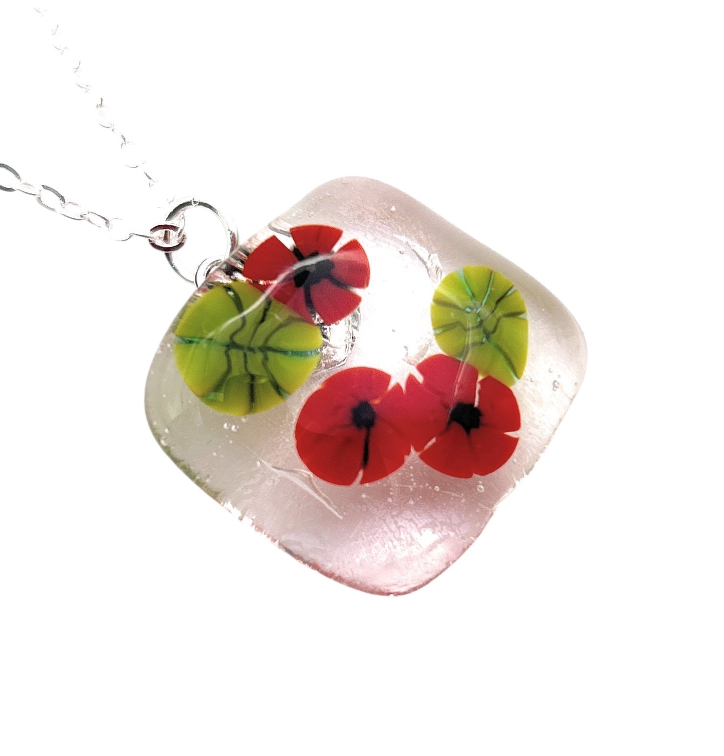 The Poppy Pendant by Calon Glass, model CGP29, is a handmade square glass pendant adorned with vibrant red and green floral designs, elegantly hanging from a silver chain. The exquisite craftsmanship of this flower pendant enhances its transparent, glossy surface.