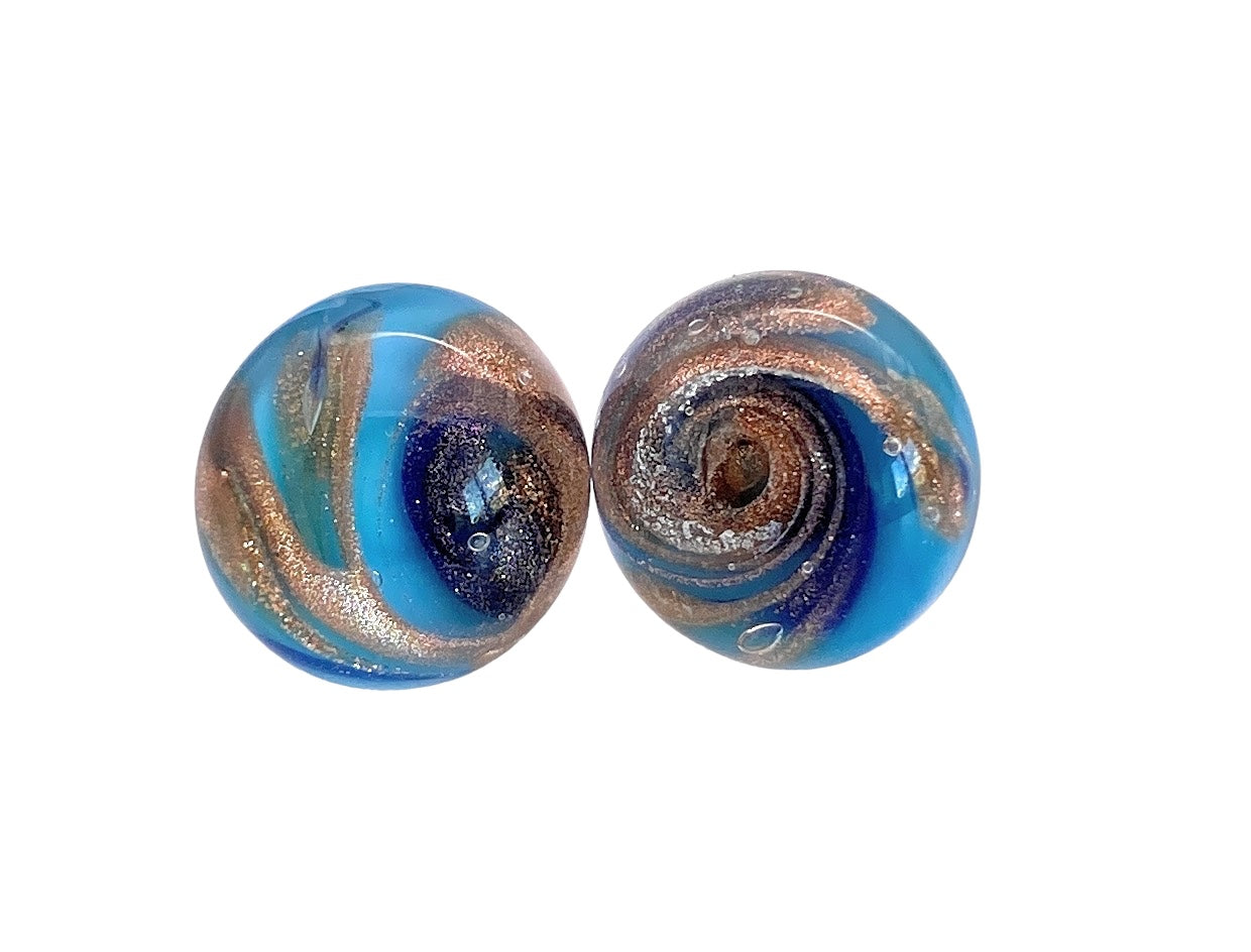 Close-up of two round glass marbles with swirling patterns. Reminiscent of Murano Passion's Murano Glass Stud Earrings with Gold Aventurine Swirls, the marbles have deep blue and metallic copper swirls that create a shimmering effect. Each appears smooth and glossy, reflecting light beautifully—a testament to their handmade craftsmanship.