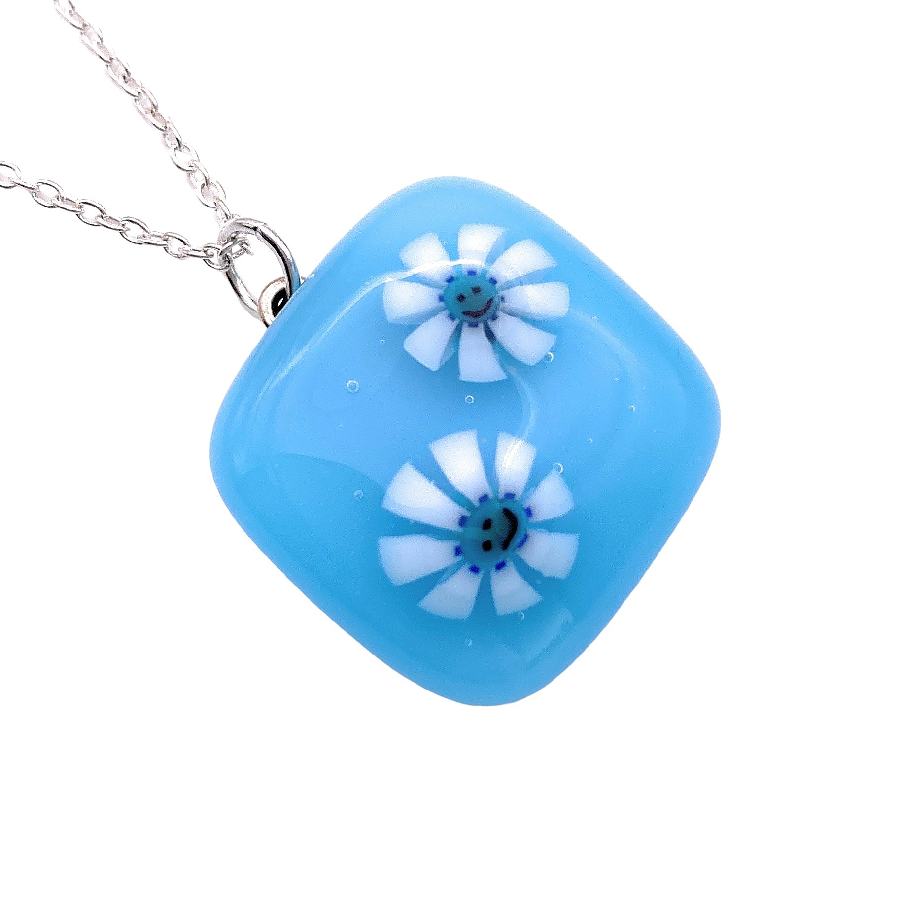 A Calon Glass Handmade Smiley Face Millefiori Flower Pendant, featuring a delicate flower design within its 2cm x 2cm blue square glass, is elegantly attached to a silver chain.