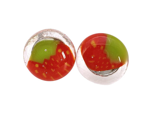 The Calon Glass Handmade Strawberry Earrings, measuring 1.5cm, feature two round glass beads with a clear outer layer that encases vibrant red and green swirls, reminiscent of intricate Millefiori glass patterns. The colors form a dynamic artistic design, with tiny air bubbles visible within these meticulously crafted earrings.