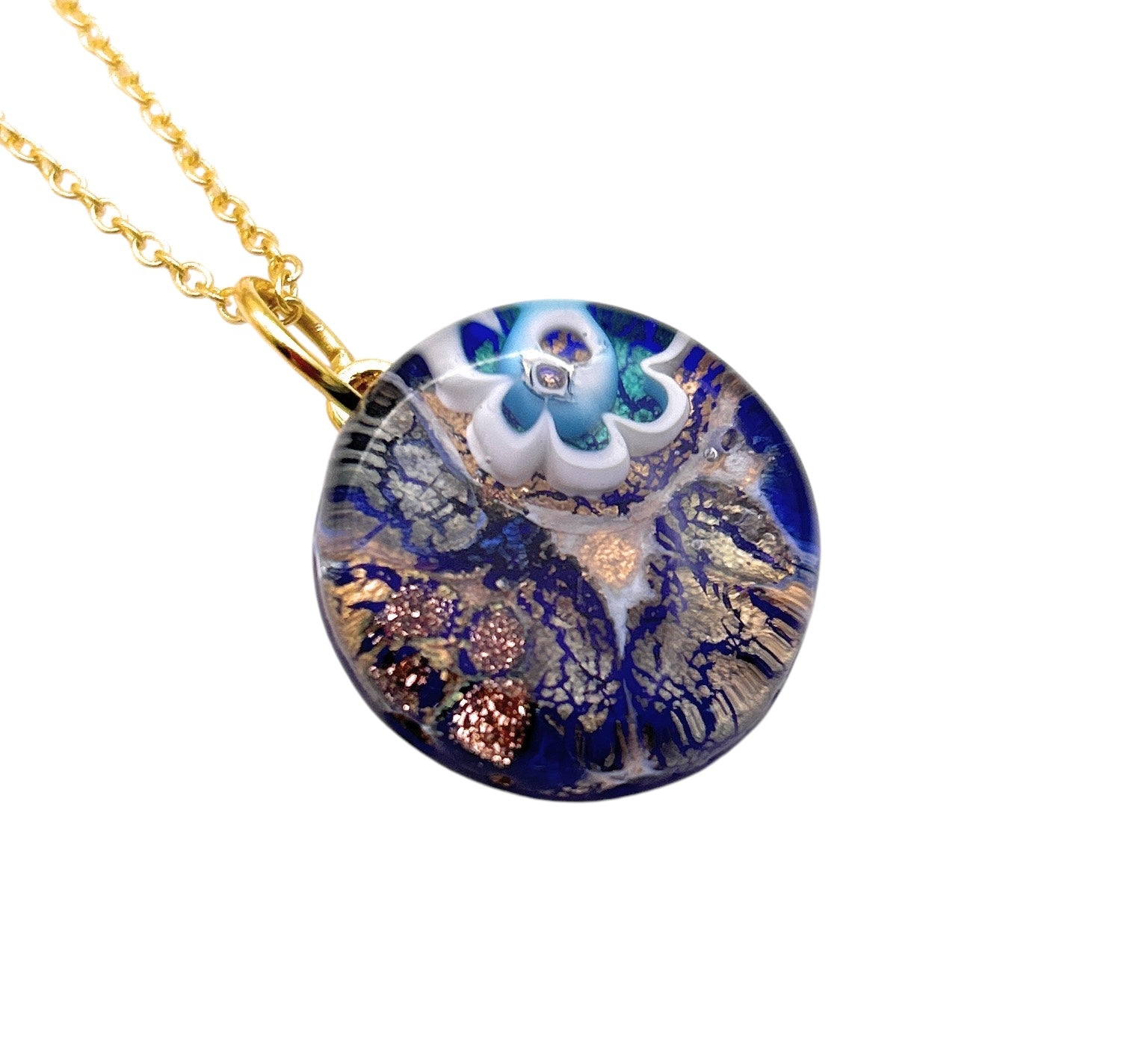 The Murano Passion piece, the Murano Glass Round Pendant made with Millefiori Flower - 2cm (MGPV20), features blue and clear glass highlighted by intricate gold and copper flecks. It flaunts a round pendant design on a gold chain, with a central floral motif in white and teal. This exquisite pendant comes complete with a Certificate of Authenticity, confirming its artisanal craftsmanship.