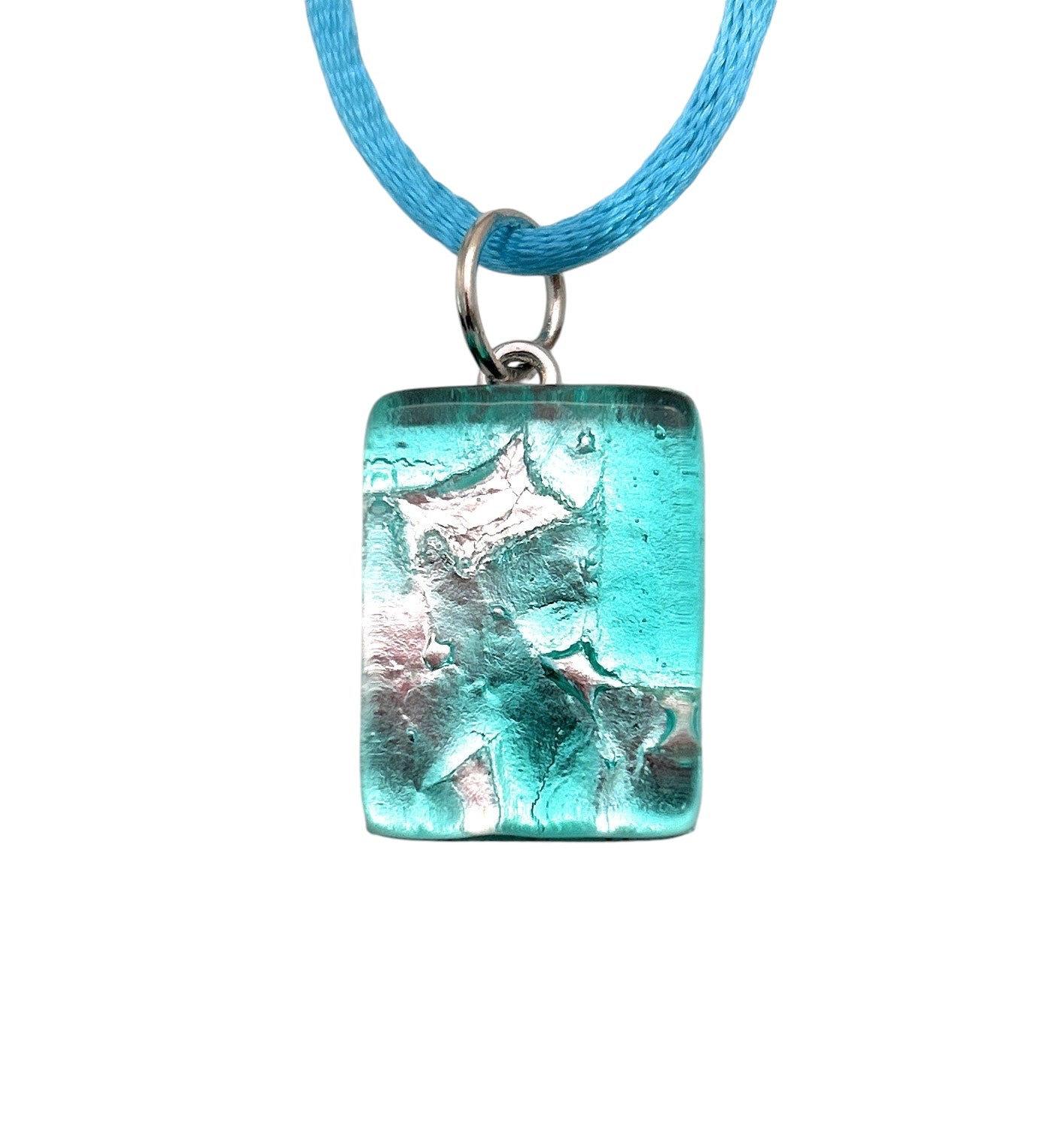 A beautiful blue cord necklace highlights the Murano Passion Murano Glass Pendant, crafted with Silver Leaf. The pendant features a rectangular design measuring 2cm x 1.5cm and showcases a translucent aqua color with silver foil accents, producing a textured effect that beautifully captures the artistry of Venetian Murano Jewelry against the white background.