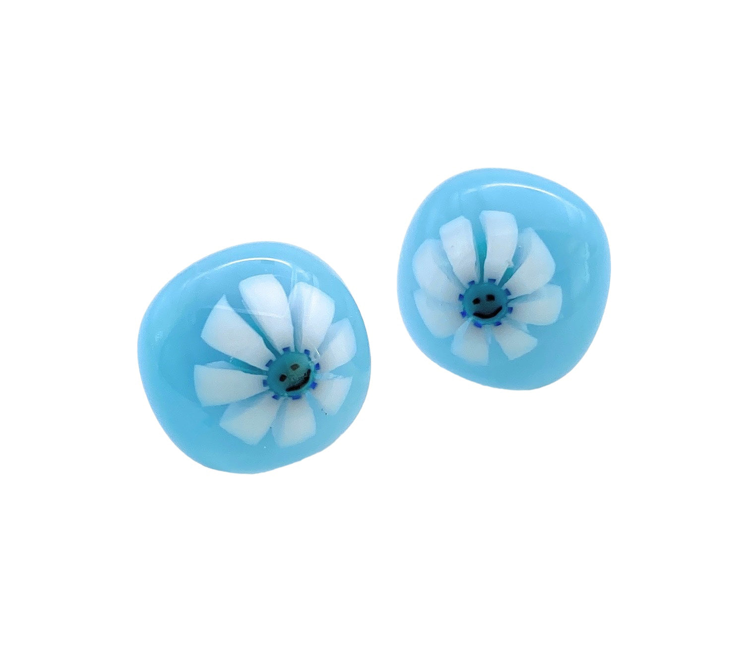 The Smiley Face Millefiori Flower Earrings by Calon Glass are exquisite handmade glass pieces featuring white flowers with multiple petals and vivid blue centers on a round, light blue background. Each stud measures 1.4cm and offers a glossy finish.