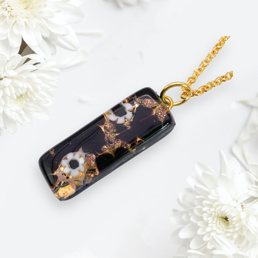 A gold chain necklace featuring the Murano Passion's Murano Glass Pendant - 3cm x 1cm Millefiori Flowers on Gold Leaf. This exquisite piece showcases a rectangular black pendant adorned with delicate white flowers and gold accents, embodying the renowned craftsmanship of Murano glass jewellery.