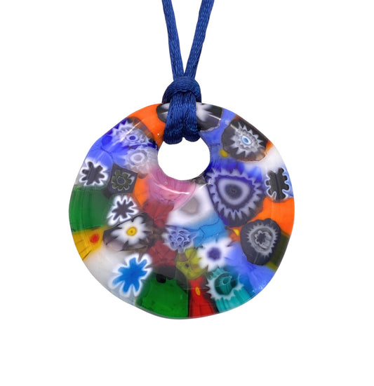 This vibrant Murano Passion Millefiori Pendant, known for its chunky 4cm diameter, showcases intricate glass flowers in blue, red, green, black, yellow, and white on a blue cord for a stunning kaleidoscopic effect.