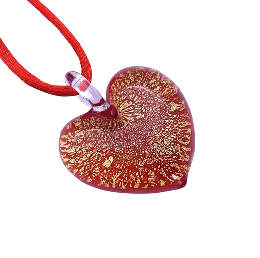 The Murano Passion Murano Glass Heart Pendant (MHT11) exudes elegance with its intricate golden patterns and is secured by a red cord. Its radiant appearance gives it a delicate, handcrafted charm. This blown glass heart pendant captures the timeless allure of Murano Glass Jewellery and is set against a plain white background.