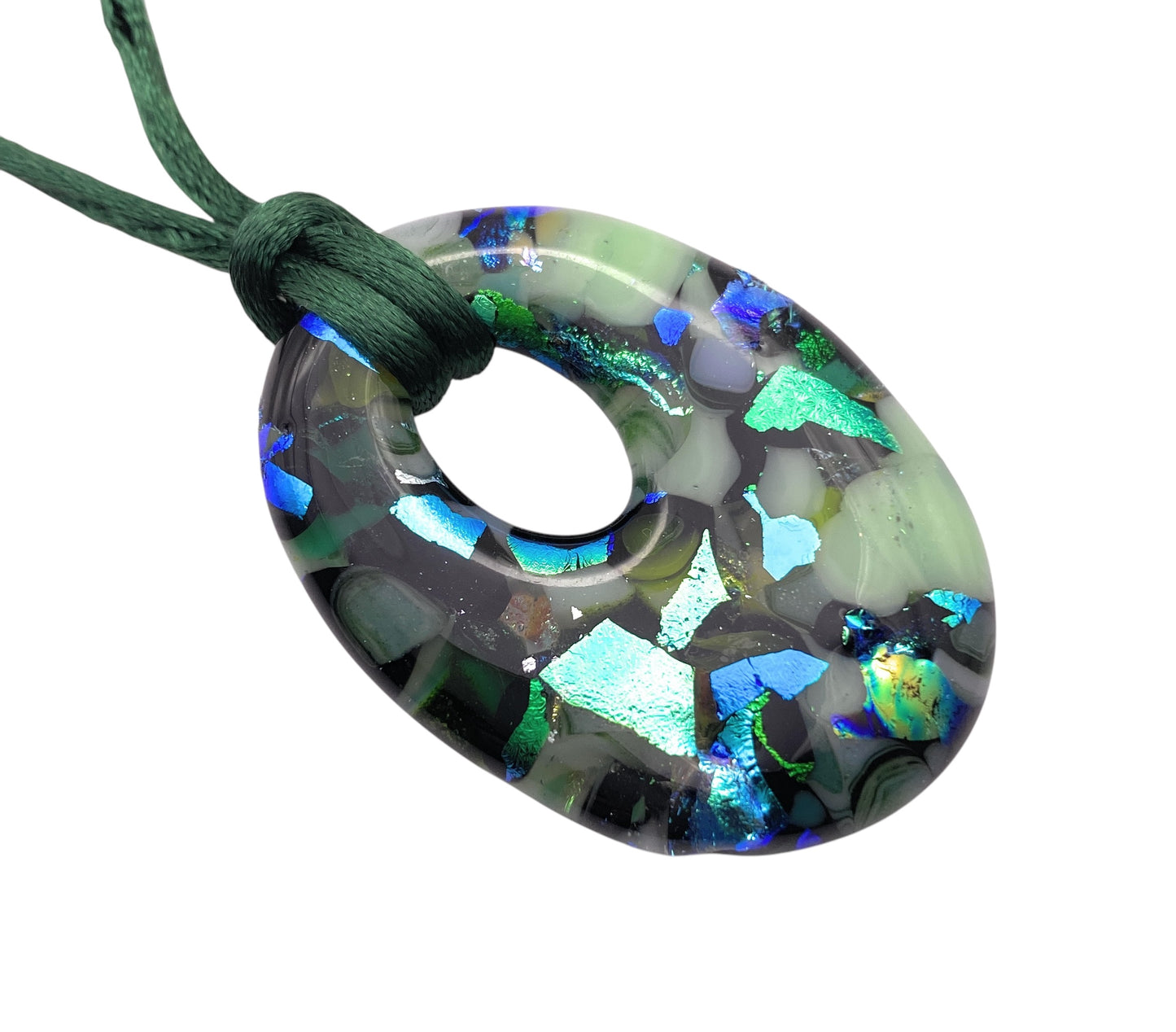 The Calon Glass Handmade Dichroic Glass Pendant (CGP34) is a 4cm x 3cm centerpiece with a circular hole, showcasing handmade dichroic glass in shades of blue, green, and black. It hangs on a dark green cord.