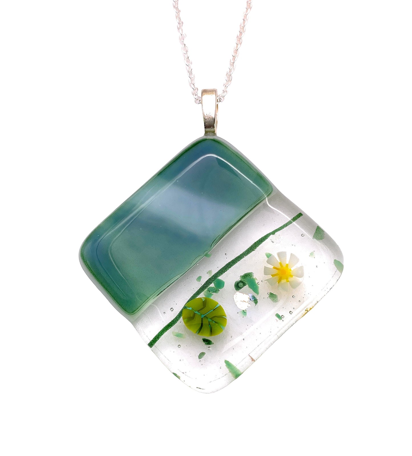 The Calon Glass Handmade Dichroic Glass Pendant, a chunky 4cm x 4cm piece, features a square of Millefiori glass adorned with delicate yellow and white floral designs set against green and clear hues. It hangs elegantly from a fine silver chain, highlighting its modern and artistic style.