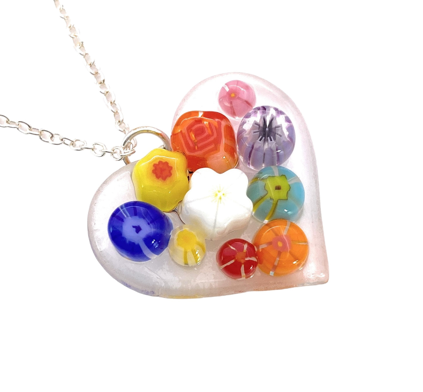 The Handmade Glass Heart Pendant by Calon Glass, measuring a dainty 2.5cm, features handmade Millefiori floral and abstract pattern beads in various shapes and designs hanging from a silver chain, giving it a vibrant and artistic look.