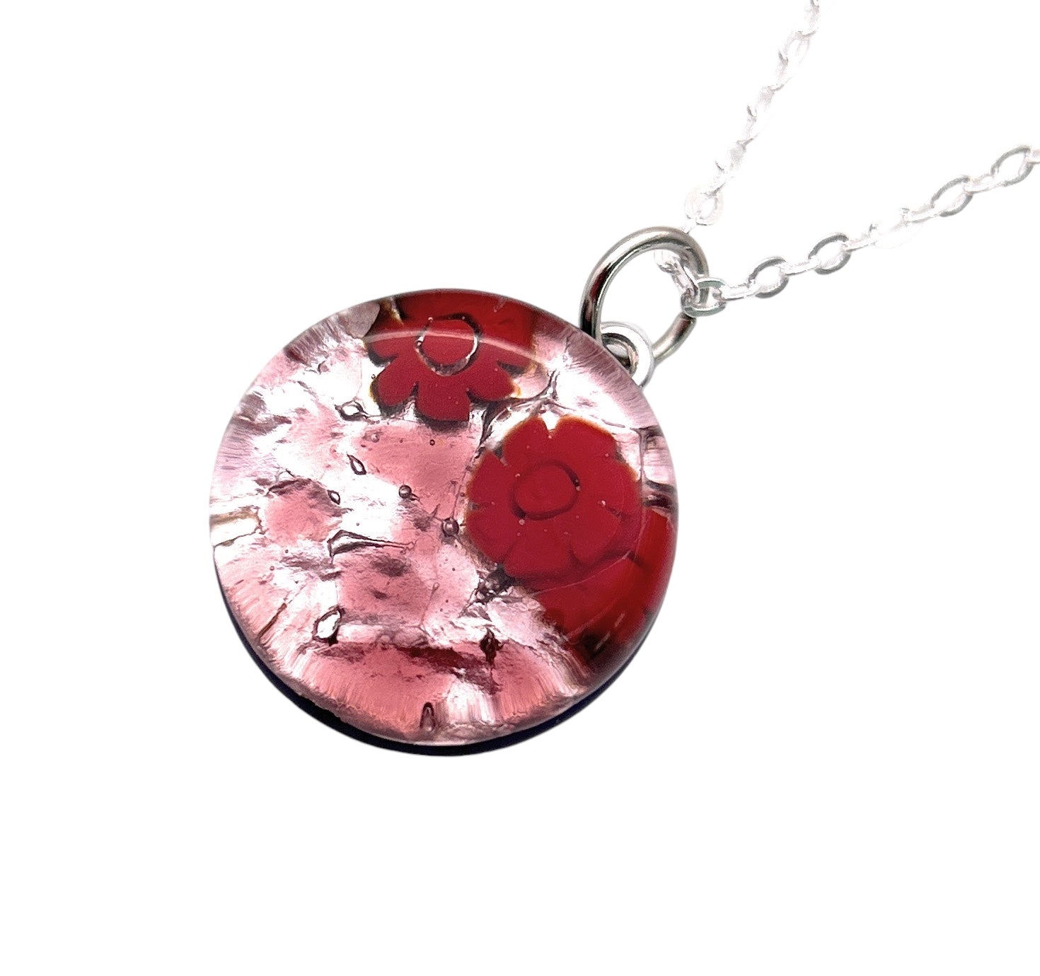 This exquisite Murano Passion necklace showcases a Murano Glass Round Pendant (MGPV19), featuring vibrant red Millefiori Flowers with delicate pink accents enclosed within a clear glass surface. The pendant, measuring 2cm, is elegantly suspended from a fine silver chain. A Certificate of Authenticity ensures the craftsmanship and origin of this remarkable piece.