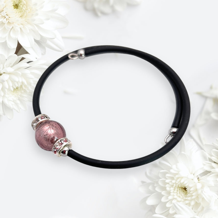 Surrounded by white chrysanthemum flowers on a light background, the Murano Glass Bead Bracelet from Murano Passion, featuring a handmade memory wire design with a 1cm pink Murano glass bead and silver accents, exudes elegance.