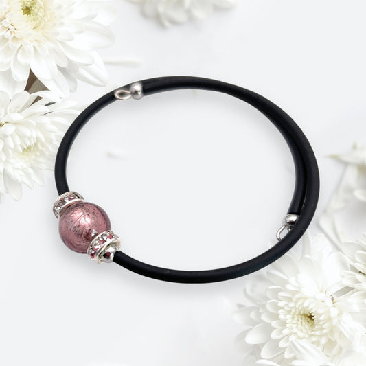 Surrounded by white chrysanthemum flowers on a light background, the Murano Glass Bead Bracelet from Murano Passion, featuring a handmade memory wire design with a 1cm pink Murano glass bead and silver accents, exudes elegance.