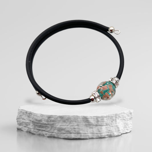 A sleek Murano Passion bracelet, featuring a single marbled 1cm Murano Glass bead on a minimalist band, is elegantly showcased on a textured white stone surface against a neutral backdrop.