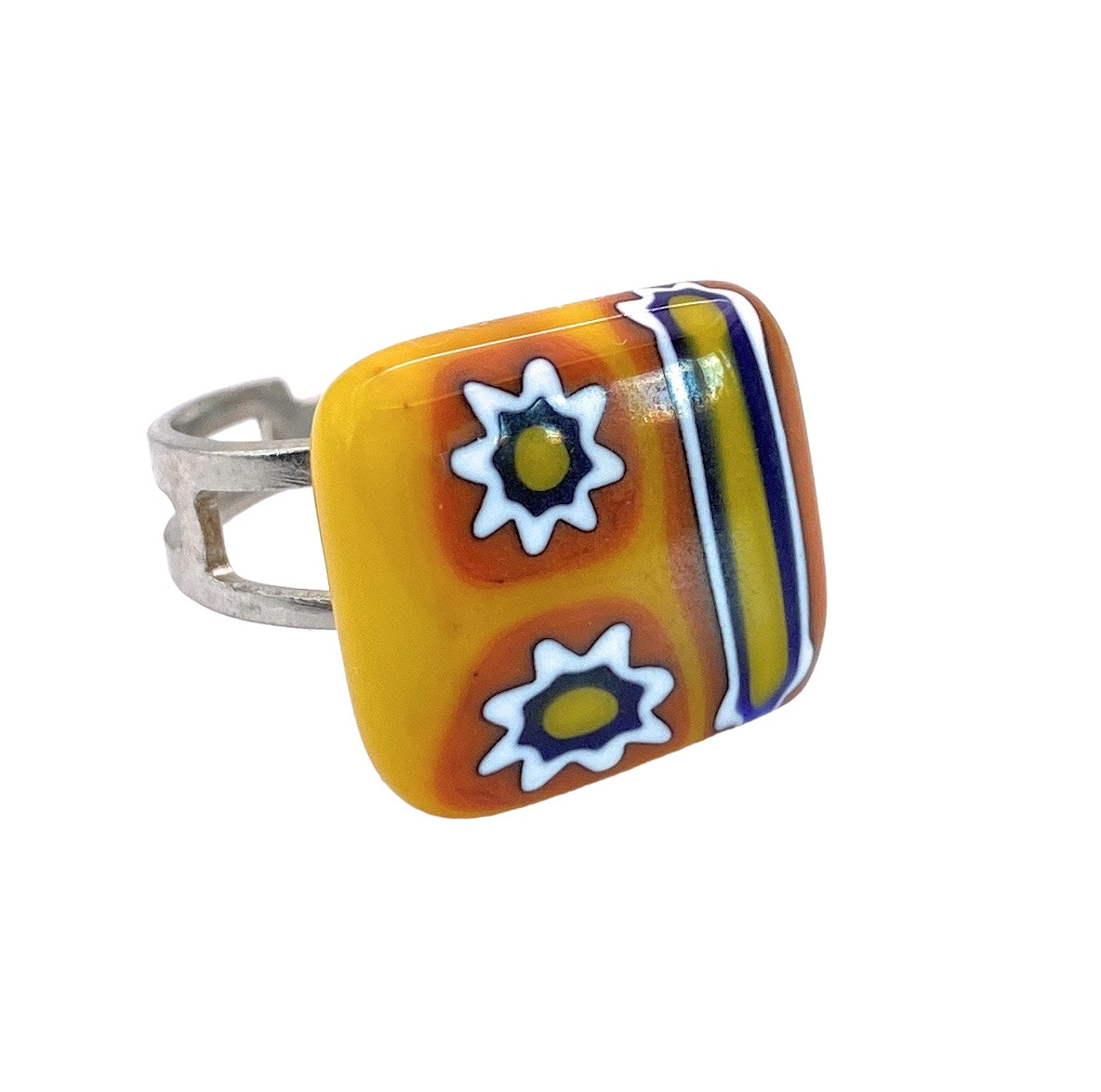 This Murano Passion Millefiori Ring features a silver band and a colorful square face. The design highlights two Millefiori glass flowers with white, star-like petals against an orange backdrop, complemented by blue, yellow, and white stripes—an homage to Venetian artistic heritage. The ring is dainty with dimensions of 1.5 cm.