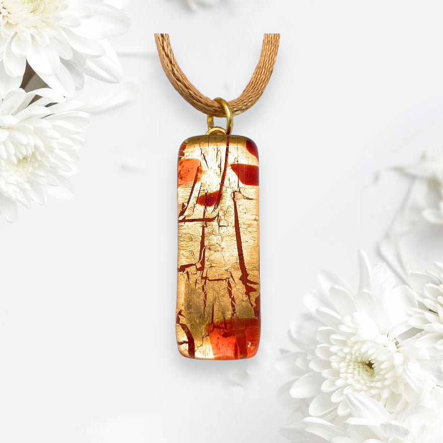 A beautifully crafted Murano Passion Gold Leaf Murano Glass Pendant (3cm x 1cm, model MGPL7) in stunning gold and red hues with a cracked pattern gracefully hangs from a brown cord, surrounded by white flowers on a light background. Its exquisite beauty is complemented by the assurance of quality provided by its Certificate of Authenticity.