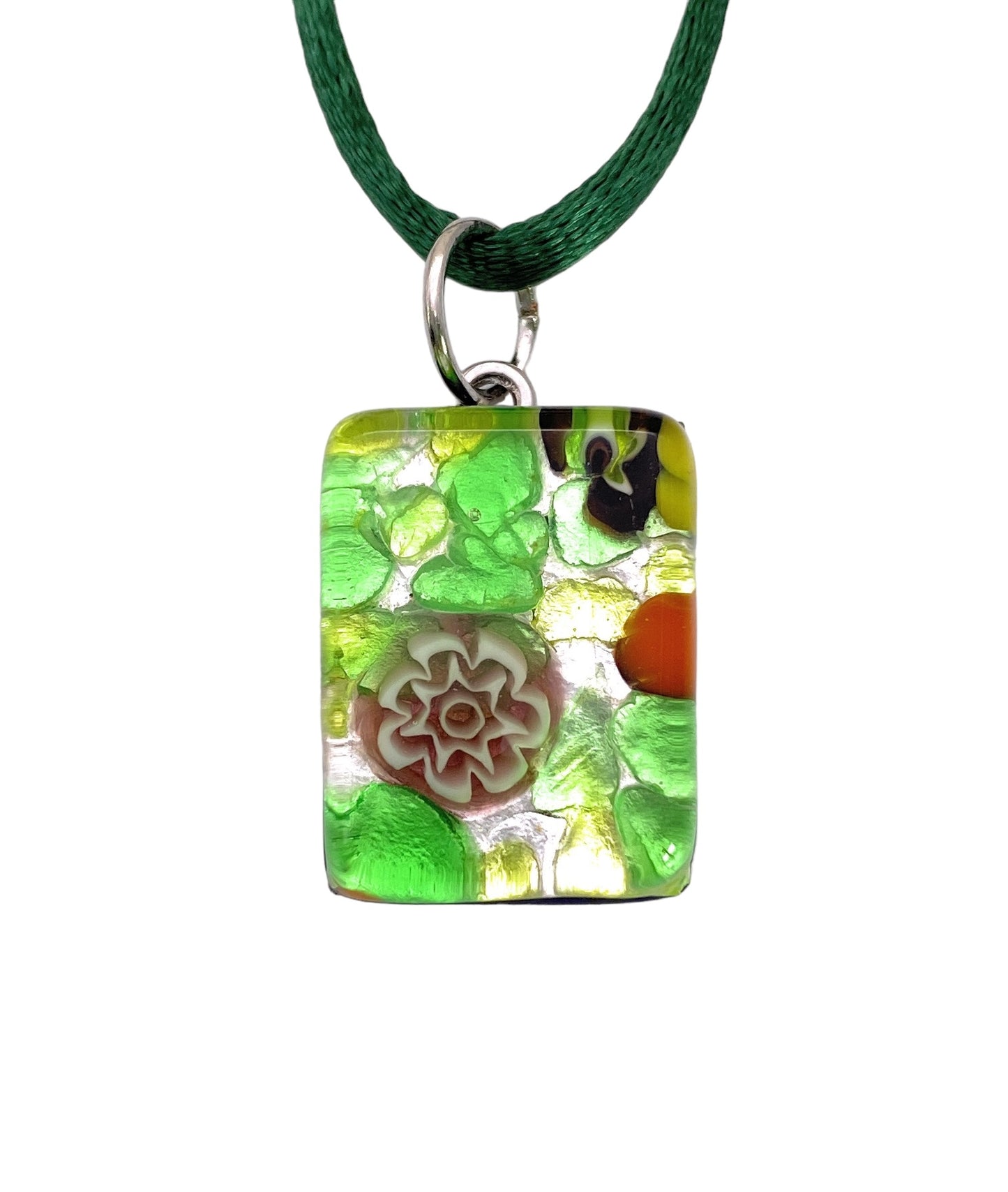 The Murano Passion pendant, Millefiori Flowers on Silver Leaf - Dainty 2cm x 1.5cm (MGPP17), highlights a rectangular design featuring a green textured background adorned with a central floral motif in white and red. Accompanied by a green cord and silver loop, this exquisite piece of Murano Glass Jewellery includes a Certificate of Authenticity.