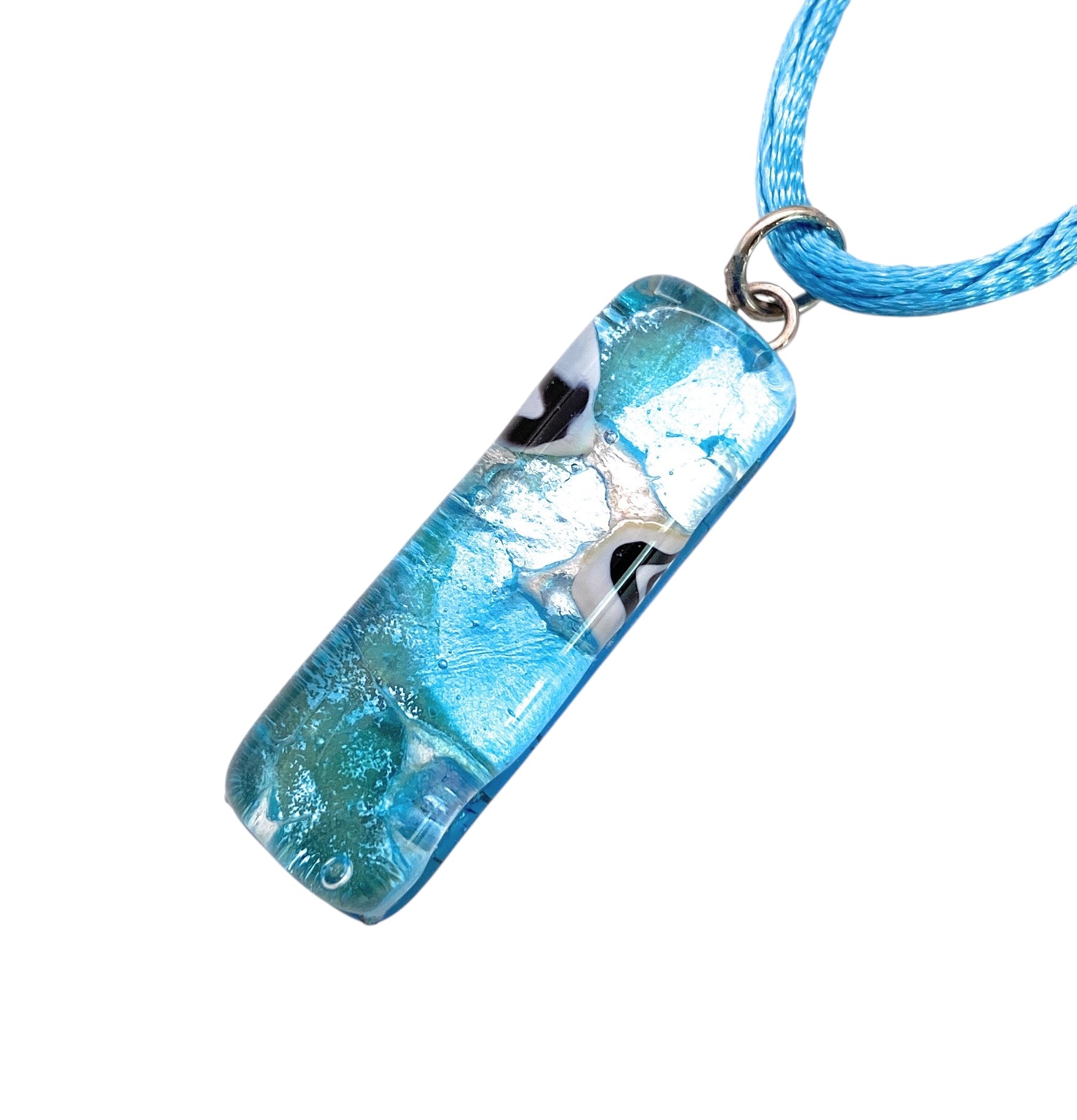 The Murano Glass Pendant on Silver Leaf - 3cm x 1cm (MGPL14) by Murano Passion, features a rectangular blue glass design with abstract silver and black patterns hanging from a matching blue cord, beautifully showcasing the exquisite craftsmanship of Murano Glass Jewellery.