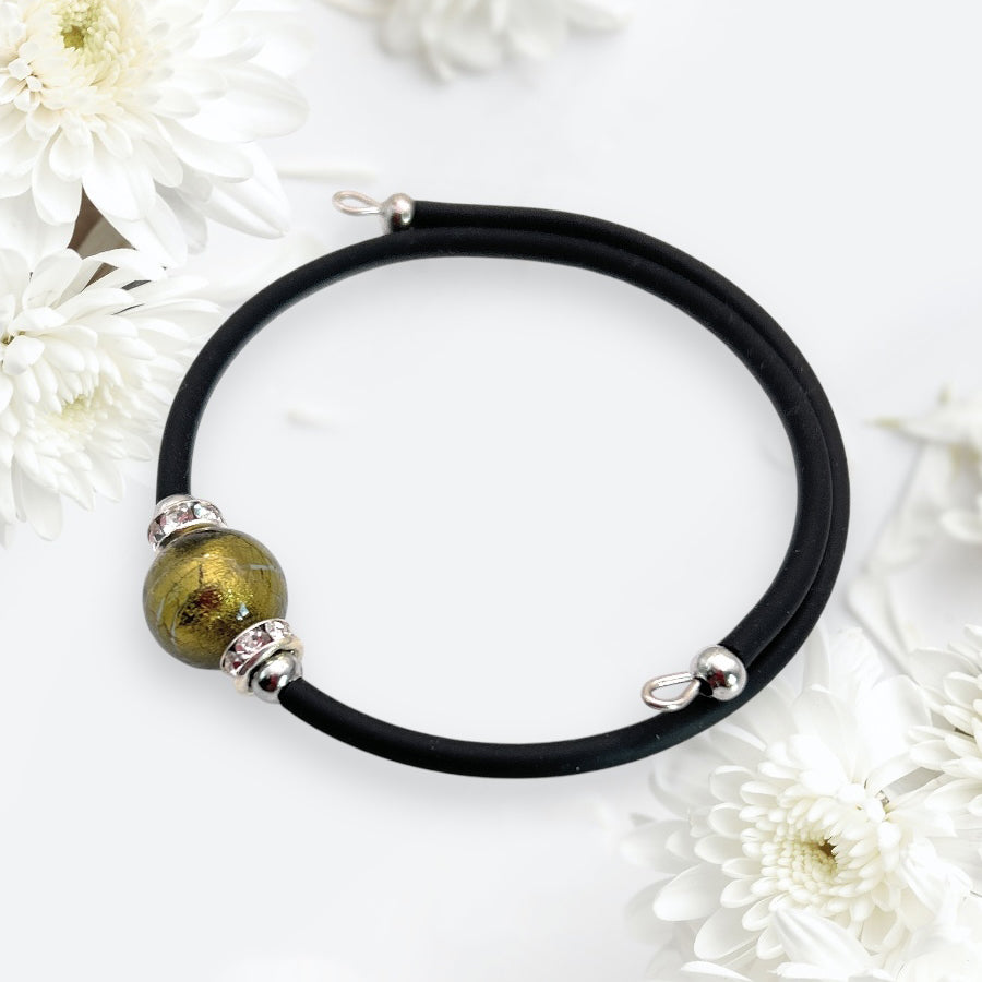 The Murano Passion Murano Glass Bead Bracelet, a handmade memory wire piece showcasing a 1cm Murano glass bead, is elegantly displayed on a white surface amidst delicate white flowers.