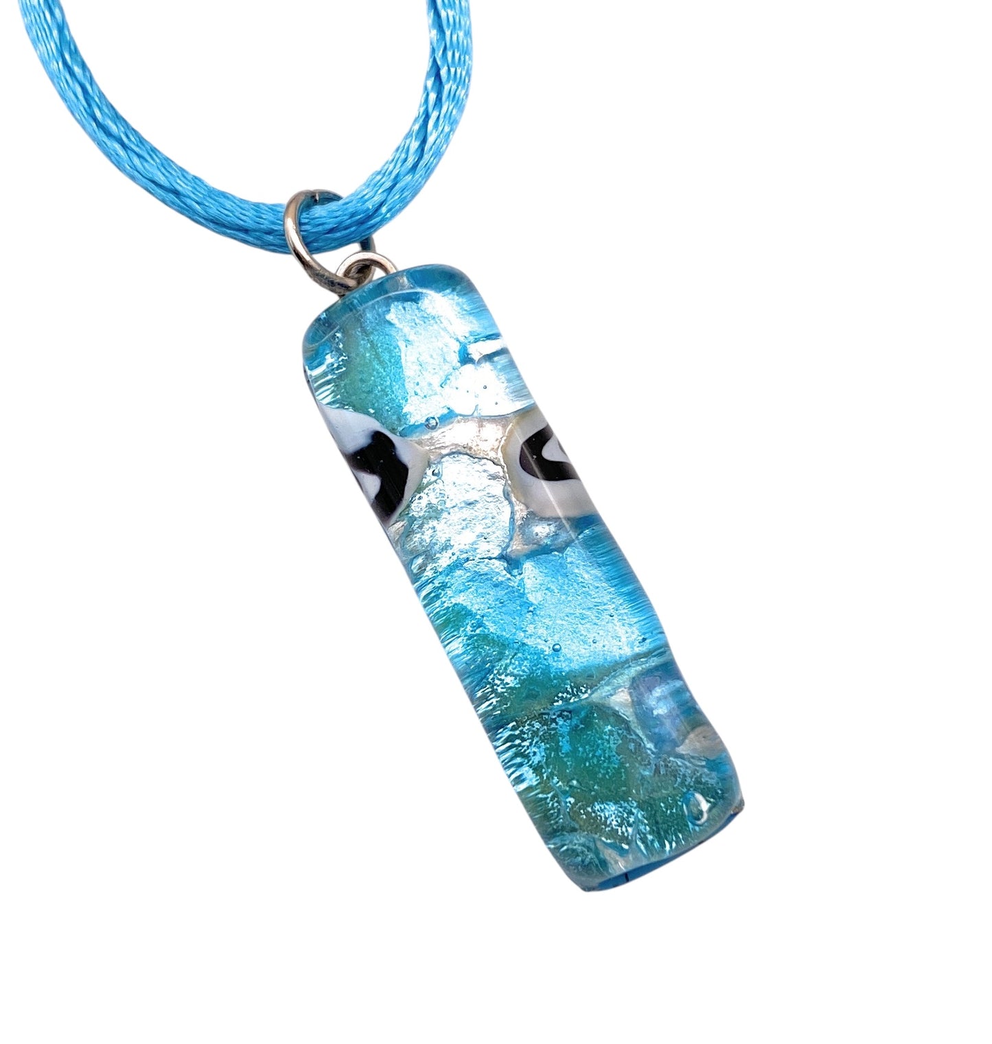 The Murano Passion Murano Glass Pendant on Silver Leaf, with its abstract white and black eye-like accents, hangs gracefully from a blue cord against a white background, showcasing elegance and charm. The pendant measures 3cm x 1cm and carries the model number MGPL14.