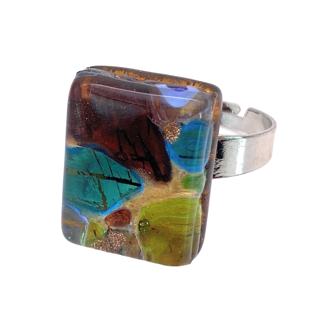 Introducing the Murano Glass Ring from Murano Passion, featuring a large, rectangular resin piece adorned with an abstract design in shades of blue, green, brown, and hints of bronze. This handmade masterpiece from Venice encapsulates the vibrant essence and authentic Italian craftsmanship reminiscent of genuine Murano Glass artistry. Dimensions: 2cm x 1.5cm.