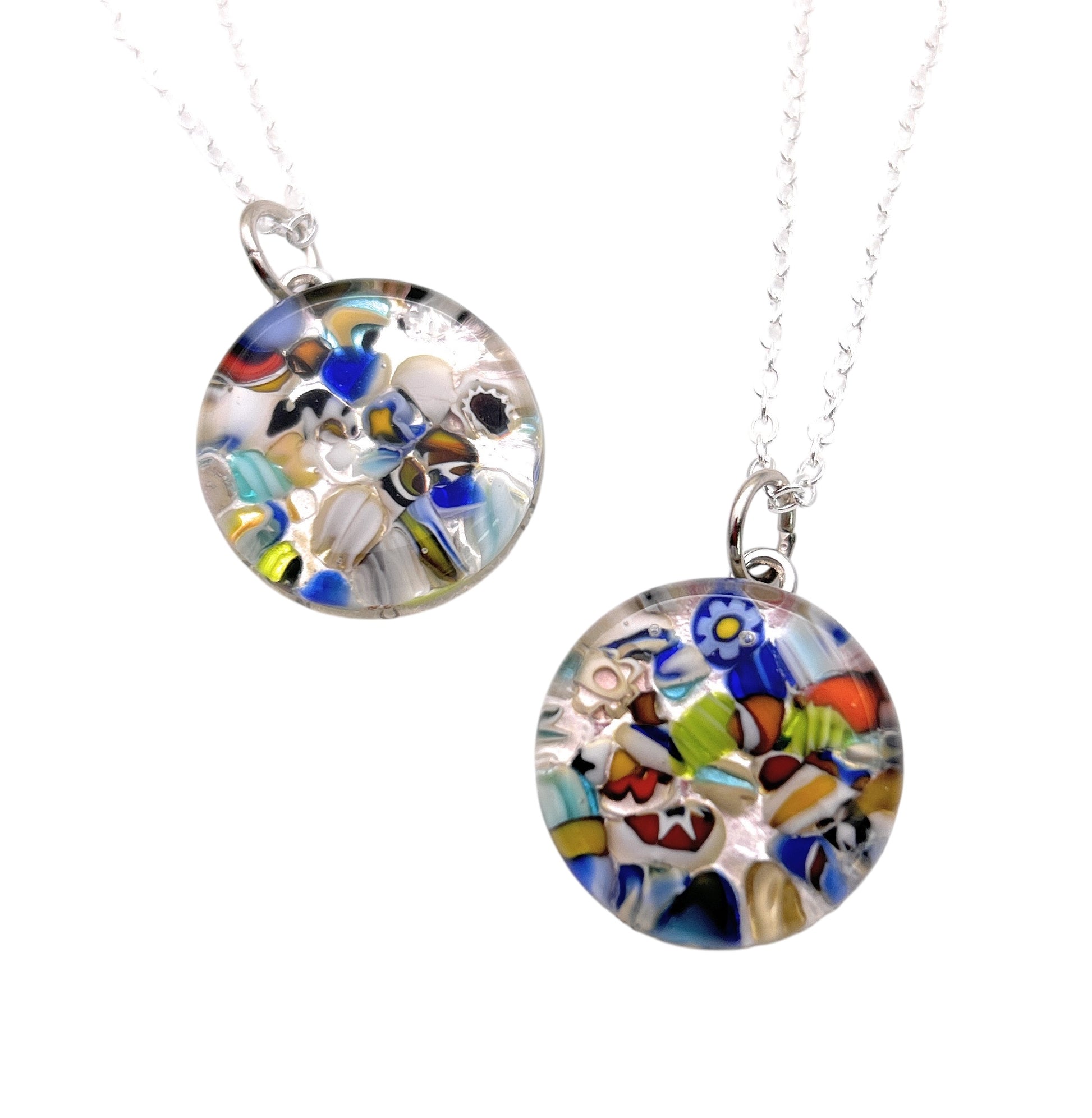 Two Murano Passion Murano Glass Round Pendants, each measuring 2cm and crafted with colorful millefiori patterns, hang from silver chains. These pendants feature intricate floral and abstract designs in vibrant blues, yellows, reds, and greens, exemplifying a unique artistic style. The purchase includes a Certificate of Authenticity for assurance.