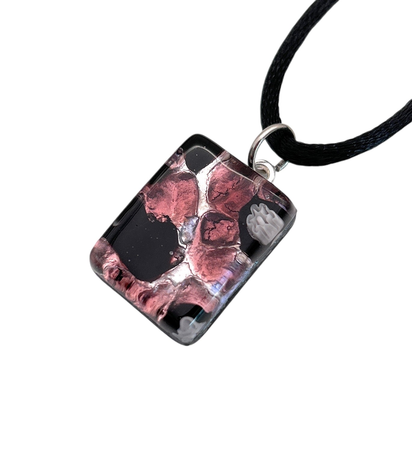 This Murano Passion pendant, named the Murano Glass Pendant - Millefiori Flower on Silver Leaf, features a dainty size of 2cm by 1.5cm and showcases exquisite craftsmanship. The piece is beautifully attached to a black cord and includes a Certificate of Authenticity to guarantee its genuine artistry.