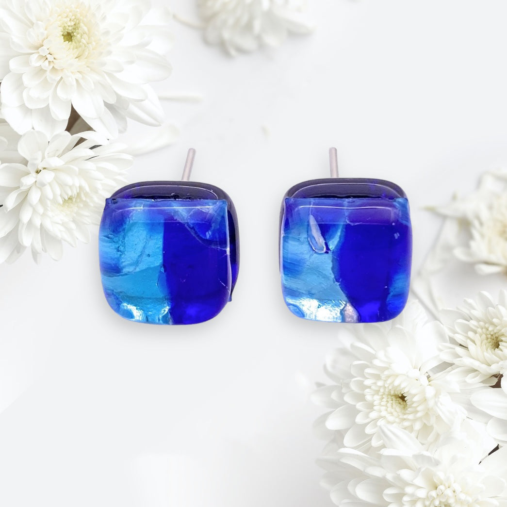 The Murano Passion earrings, featuring blue and silver Murano glass with a dainty 8mm diameter (MGE3), are showcased on a light background surrounded by white chrysanthemums.