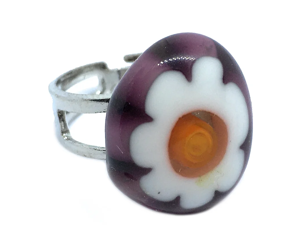 A Murano Passion silver ring showcases a large, round flower design on top. This Millefiori Flower Ring features white petals, a bright orange center, and a dark purple backdrop. The simple and adjustable band reflects Venetian artistic heritage. The ring measures 1.7cm x 1.5cm in size.