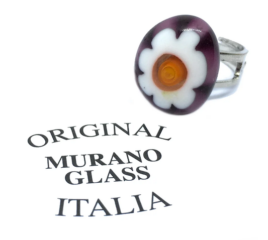 The Murano Passion Millefiori Flower Ring, a delicate piece measuring 1.7cm by 1.5cm, showcases a round flower decoration crafted from Murano glass with white petals and an orange center, honoring the rich Venetian artistic heritage. Positioned beside text proclaiming "Original Murano Glass Italia," this ring exemplifies the charm of authentic Murano glass craftsmanship.