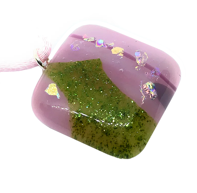 This exquisite Handmade Dichroic Glass Pendant from Calon Glass features a shiny, resin-like surface crafted with precision. A delicate light pink background highlights a sparkly green wave pattern adorned with iridescent pieces, creating a captivating design. Hanging elegantly from a pink cord, it offers a unique blend of artful charm and radiant appeal in its 2.3cm x 2.3cm form.