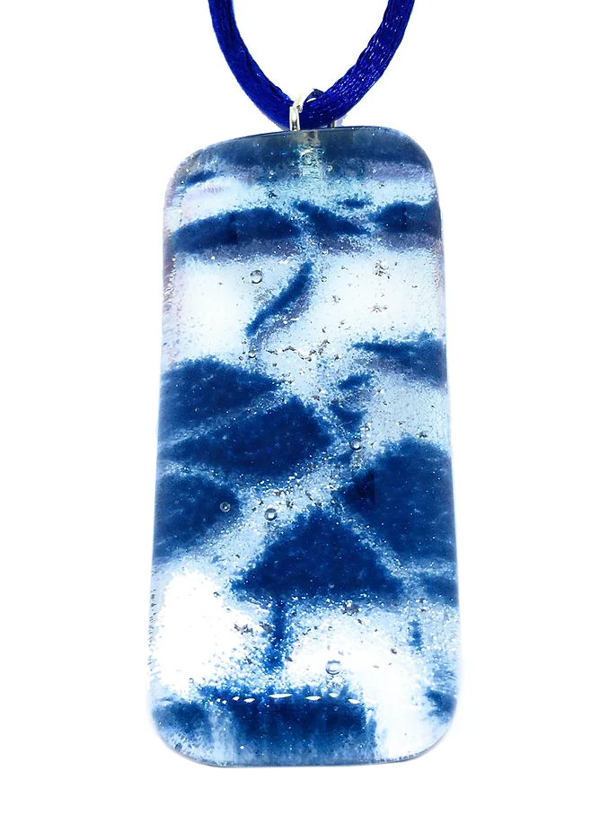 Suspended from a dark blue cord, the Dichroic Glass Pendant by Calon Glass is an elegantly handmade rectangular piece measuring 5cm x 2cm. It features swirling blue patterns against a white background, with small bubbles encapsulated within, showcasing the art of kiln-fused creations.