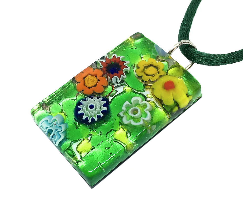 The Murano Passion Millefiori Flower Pendant, measuring 3cm by 2cm, features a vibrant design of colorful flowers in orange, yellow, red, and blue set against a lush green background on silver leaf. This striking piece of Venetian glass jewelry elegantly hangs from a coordinating green cord.