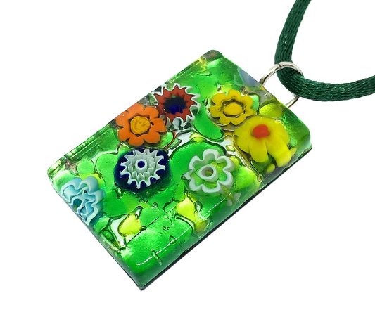 The Murano Passion Millefiori Flower Pendant, measuring 3cm by 2cm, features a vibrant design of colorful flowers in orange, yellow, red, and blue set against a lush green background on silver leaf. This striking piece of Venetian glass jewelry elegantly hangs from a coordinating green cord.