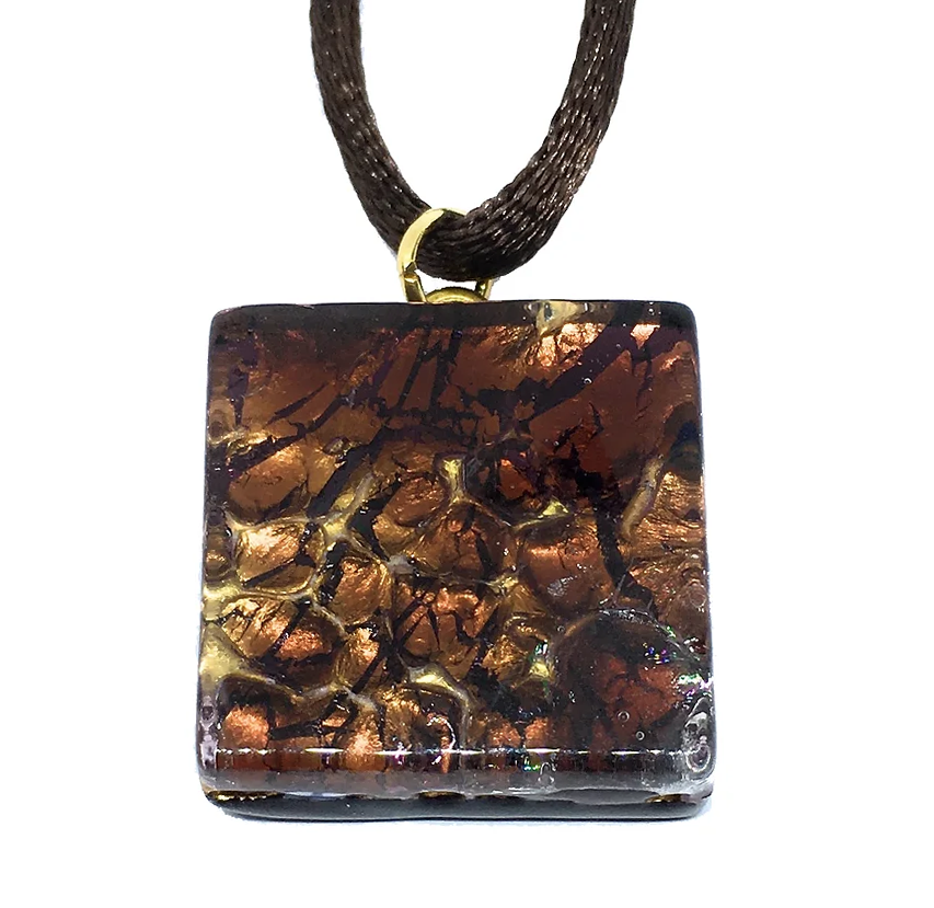 The Murano Passion pendant showcases an exquisite design of marbled copper, brown, and black tones in a square shape. It gracefully hangs from a dark, textured cord adorned with a small gold ring. This 2cm x 2cm piece is accompanied by a Certificate of Authenticity to verify its artisanal craftsmanship.