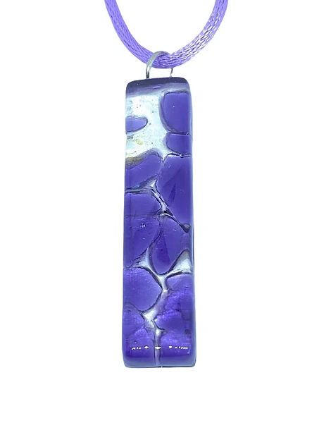 A rectangular Murano Passion Glass Pendant on Silver Leaf, measuring 4cm x 1cm, hangs on a light purple cord. The pendant boasts a floral pattern with abstract shapes in varying shades of purple and white, providing it with a textured appearance. It also comes with a Certificate of Authenticity.