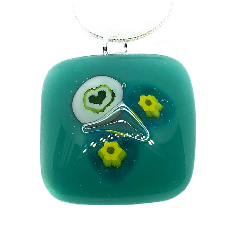 Introducing the Calon Glass Handmade Pendant, a stunning square teal piece with a 2.3cm x 2.3cm measurement. It features an abstract heart design in white and green, beautifully accented by two delicate yellow millefiori flowers. This exquisite glass creation elegantly hangs on a silver chain, making it a truly unique accessory.