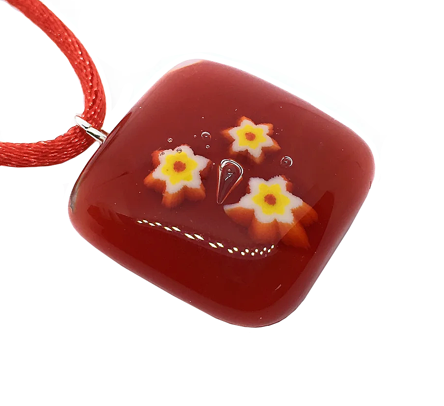 The Handmade Glass Pendant, Red with Millefiori Flowers by Calon Glass showcases a square red dichroic glass design, accented with three intricate yellow and white flower patterns. Measuring 2.3cm x 2.3cm, this pendant is attached to a red cord necklace and features a glossy finish that truly stands out.