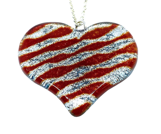 The Handmade Heart Pendant from Calon Glass showcases a heart-shaped design crafted from dichroic glass, featuring red and silver wavy stripes. Measuring 4cm by 3.5cm, it dangles from a silver chain and boasts a shiny surface with a glittery texture that creates a sparkling look.