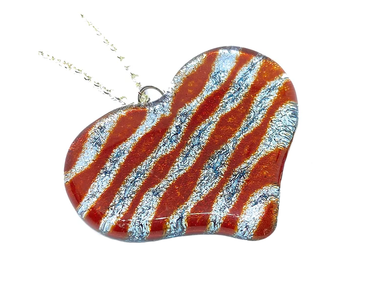 A Handmade Heart Pendant in Dichroic Glass by Calon Glass, measuring 4cm x 3.5cm, showcases a red and silver wave pattern and hangs elegantly on a delicate silver chain.