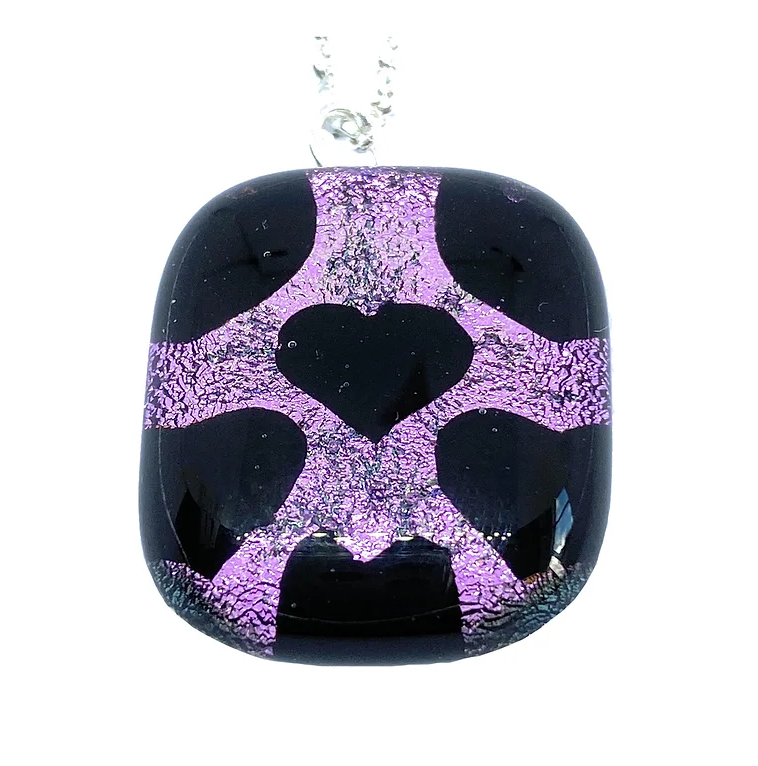 Crafted by Calon Glass, the Handmade Dichroic Glass Heart Pendant, measuring 2.5cm x 2cm, is a rectangular black piece that beautifully highlights a central heart shape in a purple metallic pattern. This intricate design of abstract lines and textures is kiln-fused to perfection and elegantly hangs from a silver chain.