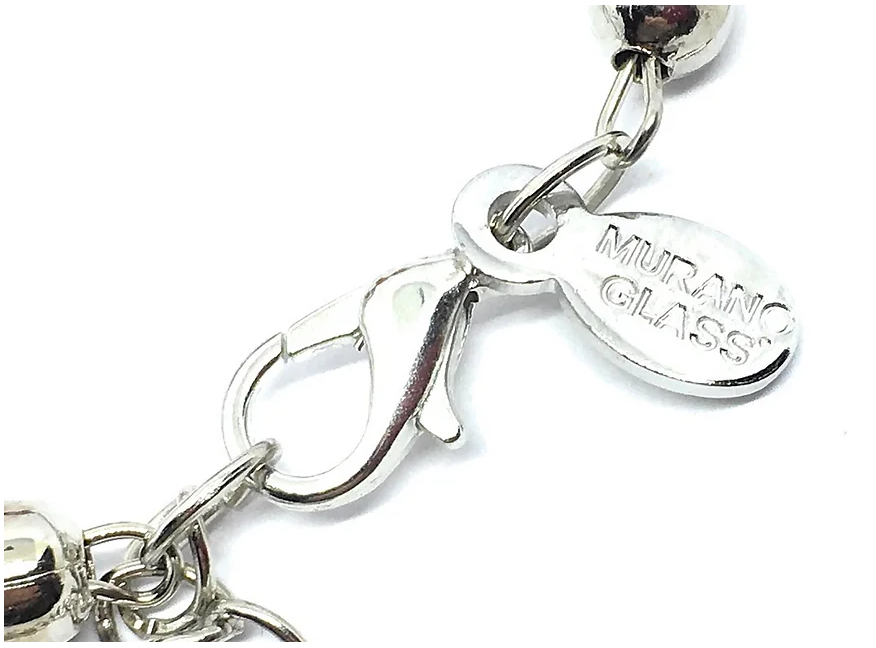 This is a close-up of a silver necklace clasp showcasing a round tag engraved with "Murano Glass," which brings to mind the elegance of our Murano Passion Bracelet. Featuring a lobster claw style clasp attached to a beaded chain, each piece is handmade and comes with its own Certificate of Authenticity.