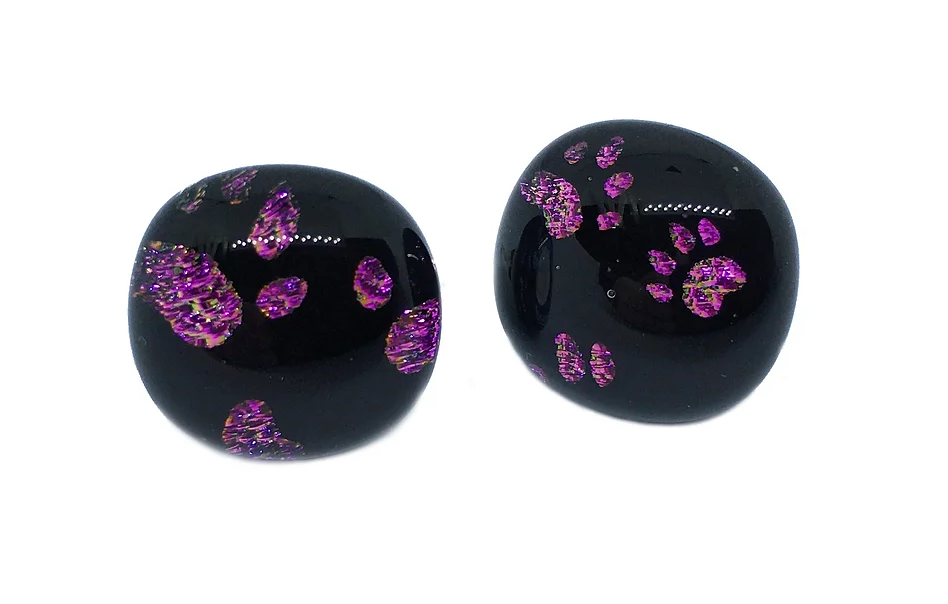 Two glossy black glass earrings with glittery purple paw print designs crafted from dichroic glass are featured against a plain white background. These are the 1.3cm Handmade Dichroic Glass Earrings by Calon Glass.