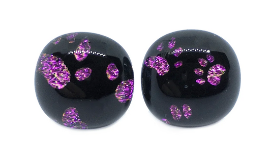 These handmade dichroic glass earrings by Calon Glass feature shiny purple glitter patterns, and their black stud design creates a decorative and elegant look.